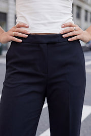 Pantalón ajustado de fit flare, cintura media con pretina, bolsillos delanteros y vivos decorativos posteriores. Cierre frontal con broche y cremallera ocultos.