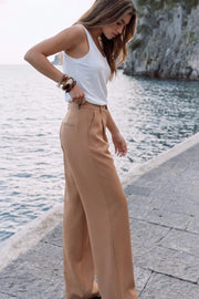 Pantalón de fit wide leg, cintura alta con pretina y trabillas, pinzas frontales, bolsillos delanteros y vivos decorativos posteriores. Cierre frontal con botón y cremallera oculta.