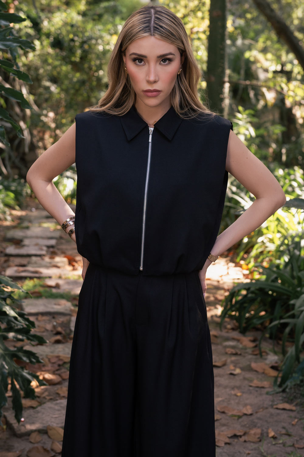 Pantalón de fit wide leg, cintura media con pretina, trabillas ajustables laterales, pinzas frontales, bolsillos delanteros y vivos decorativos posteriores. Cierre frontal con broche y cremallera ocultos.