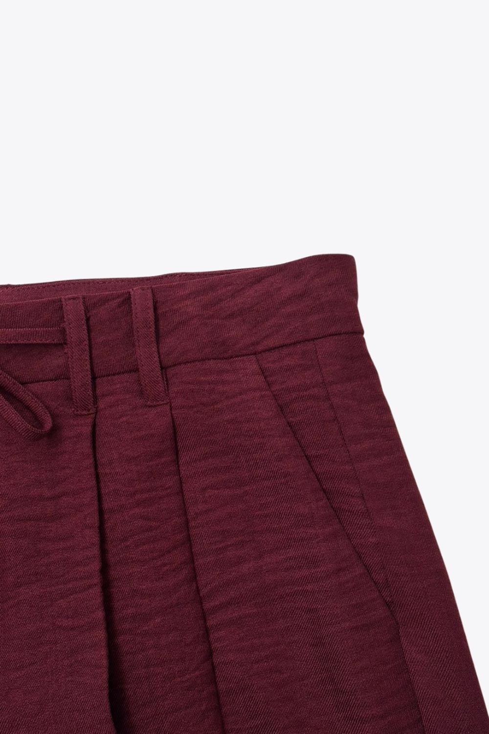 Pantalón de fit wide leg, cintura alta con pretina, trabillas y lazo amarrable en cintura, pinzas frontales y bolsillos delanteros. Cierre frontal con broche y cremallera oculta.