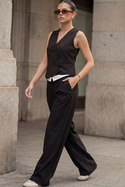 Pantalón de fit wide leg, pinzas frontales, cintura media, pretina con detalle de tailoring en contraste, bolsillos delanteros y vivos decorativos posteriores. Cierre frontal con broche y cremallera ocultos.