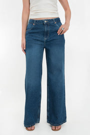 Pantalón wide leg de denim, cintura alta con pretina y trabillas, bolsillos delanteros y posteriores de parche. Cierre frontal con botón y cremallera oculta.
