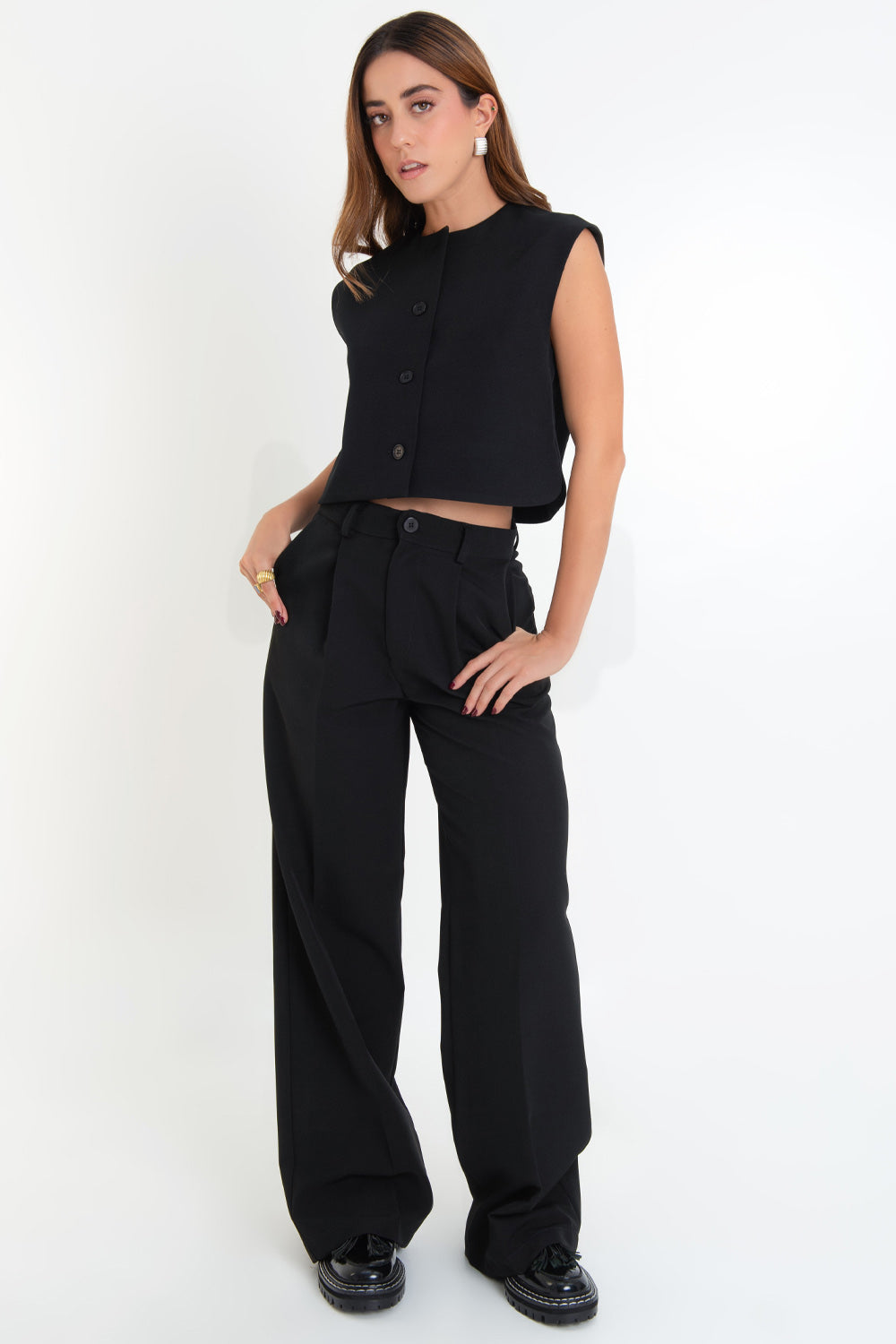 Pantalón de fit wide leg, cintura alta con pretina y trabillas, bolsillos delanteros y vivos decorativos posteriores, pinzas delanteras, raya frontal y posterior, cierre frontal con botón y cremallera oculta.