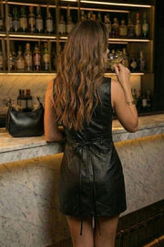 Playsuit de efecto piel, fit ajustado, cuello barco, sin mangas, pinzas frontales, lazo amarrable posterior y cierre con cremallera oculta.