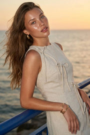 Playsuit de lino, fit ajustado, cuello barco, sin mangas, pinzas frontales, lazo amarrable posterior y cierre con cremallera oculta. Detalle frontal de lazos decorativos.