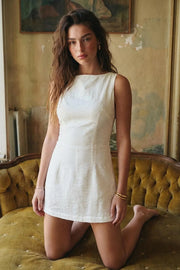 Playsuit de fit ajustado, cuello barco, sin mangas, pinzas frontales, lazo amarrable posterior y cierre con cremallera oculta.