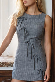 Playsuit de estampado rayas, fit ajustado, cuello barco, sin mangas, pinzas frontales, lazo amarrable posterior y cierre con cremallera oculta. Detalle frontal de lazos decorativos.