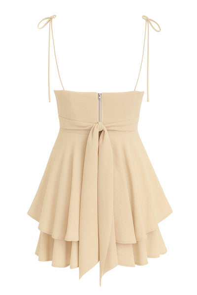 Playsuit de tirantes delgados con nudo amarrable, escote v con detalles plisados y lazo decorativo frontal, pretina cruzada frontal con lazo amarrable posterior y capas de olanes en bajo. Cierre posterior con cremallera visible en contraste.