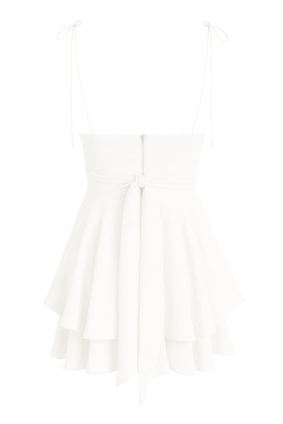 Playsuit de tirantes delgados con nudo amarrable, escote v con detalles plisados y lazo decorativo frontal, pretina cruzada frontal con lazo amarrable posterior y capas de olanes en bajo. Cierre posterior con cremallera visible en contraste.