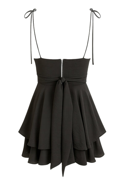 Playsuit de tirantes delgados con nudo amarrable, escote v con detalles plisados y lazo decorativo frontal, pretina cruzada frontal con lazo amarrable posterior y capas de olanes en bajo. Cierre posterior con cremallera visible en contraste.