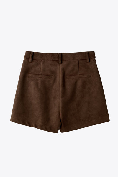 Short corto de gamuza, fit recto, cintura alta con pretina y trabillas, bolsillos delanteros y vivos decorativos posteriores. Detalle de pinzas frontales, cierre frontal con broche y cremallera ocultos.