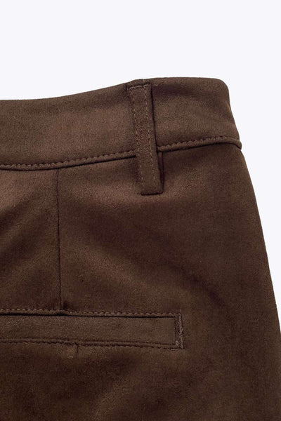 Short corto de gamuza, fit recto, cintura alta con pretina y trabillas, bolsillos delanteros y vivos decorativos posteriores. Detalle de pinzas frontales, cierre frontal con broche y cremallera ocultos.