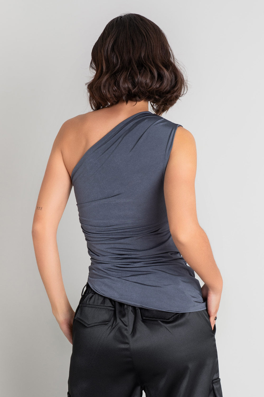 Top asimétrico de fit ajustado, sin mangas, plisados en un hombro y costados, escote diagonal y bajo curveado asimétrico.
