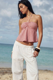 Top corto de estampado rayas, cuello halter con lazo amarrable posterior, escote corazón con jareta ajustable y plisados frontales. Detalle de peplum con olanes y fruncido en espalda.