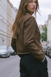 Top blazer corto de fit fluido, manga larga, escote v con solapa y cierre frontal con lazos amarrables. Detalle de ribete decorativo en contraste.