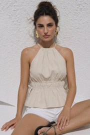 Top corto de cuello halter con plisados, tirantes delgados, detalle de rib con plisados y lazos laterales en costados, peplum con olanes en bajo y cierre posterior con botón y ojal.