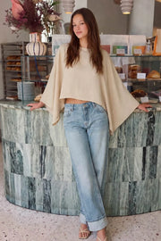 Blusa satinada tipo capa de fit fluido, manga larga amplia, cuello barco y bajo asimétrico.