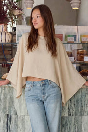 Blusa satinada tipo capa de fit fluido, manga larga amplia, cuello barco y bajo asimétrico.
