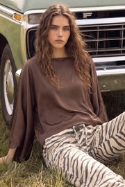 Blusa satinada tipo capa de fit fluido, manga larga amplia, cuello barco y bajo asimétrico.
