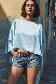 Blusa satinada tipo capa de fit fluido, manga larga amplia, cuello barco y bajo asimétrico.