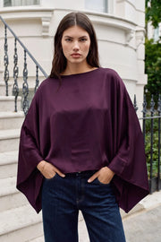 Blusa satinada tipo capa de fit fluido, manga larga amplia, cuello barco y bajo asimétrico.