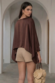 Blusa satinada tipo capa de fit fluido, manga larga amplia, cuello barco y bajo asimétrico.