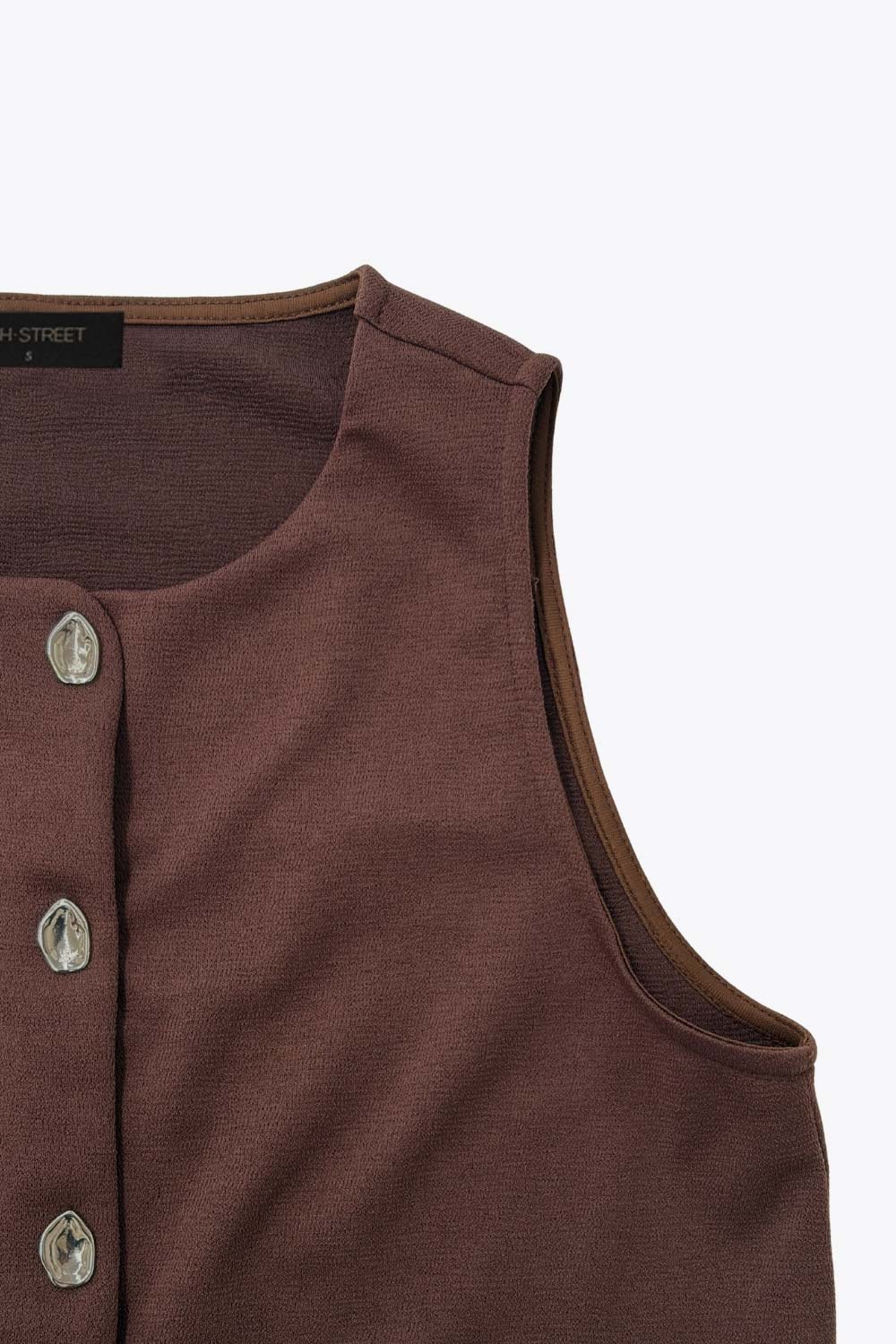 Chaleco corto de fit recto, cuello redondo y cierre frontal con hilera de botones en contraste. Detalle abertura v en bajo.