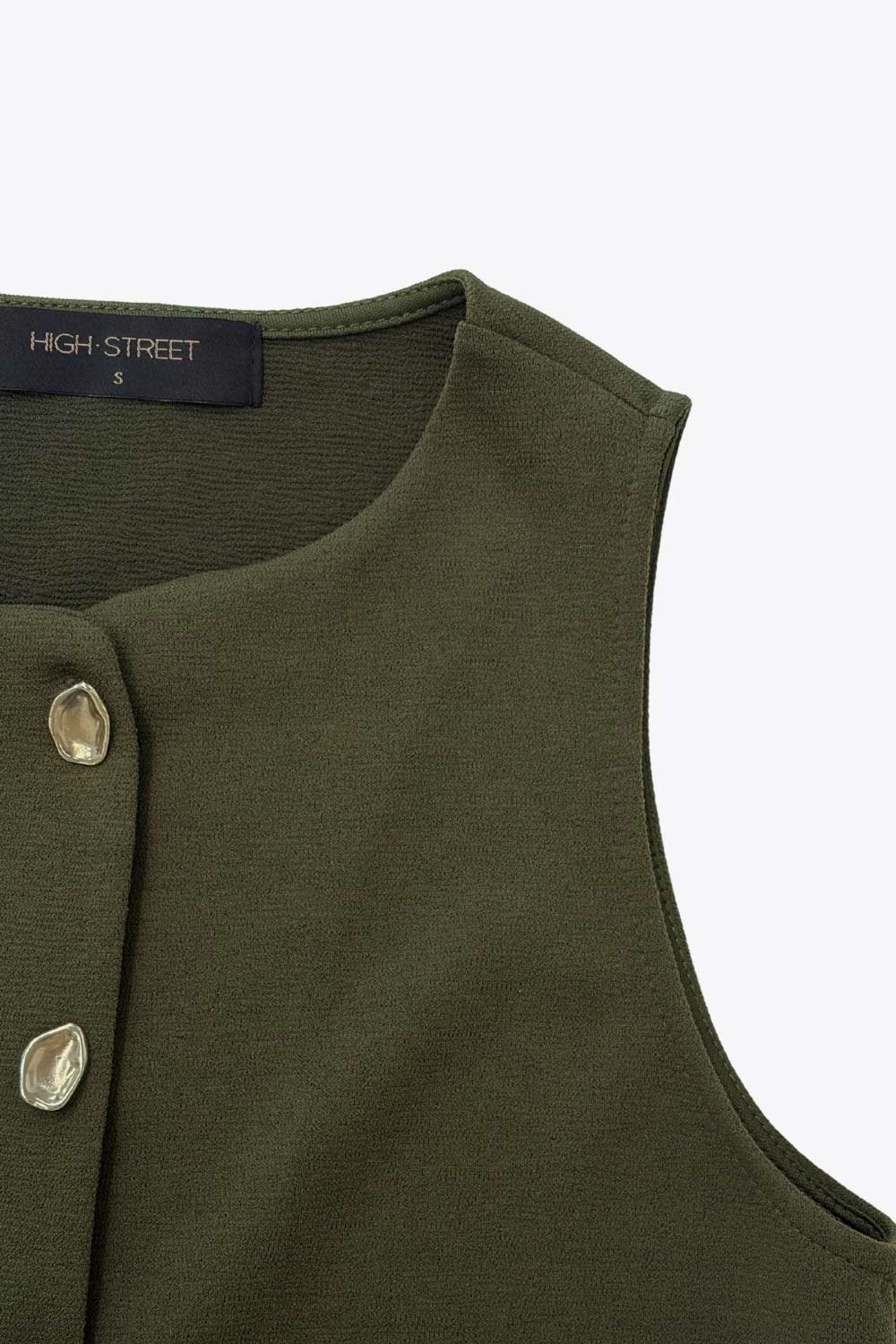 Chaleco corto de fit recto, cuello redondo y cierre frontal con hilera de botones en contraste. Detalle abertura v en bajo.