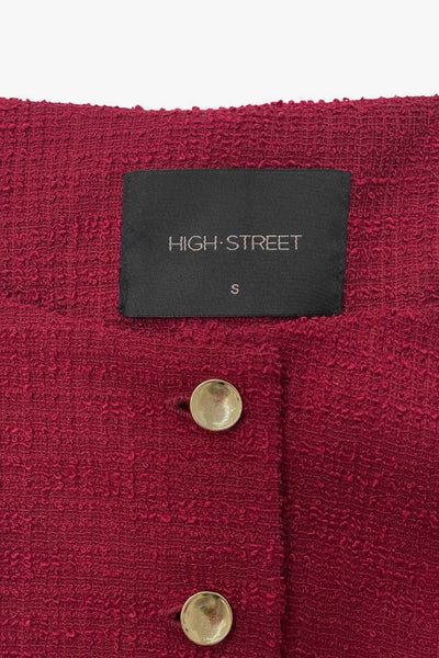 Chaleco corto de bouclé, fit recto, cuello barco y cierre frontal con hilera de botones en contraste. Detalle abertura v en bajo y vivos decorativos frontales.