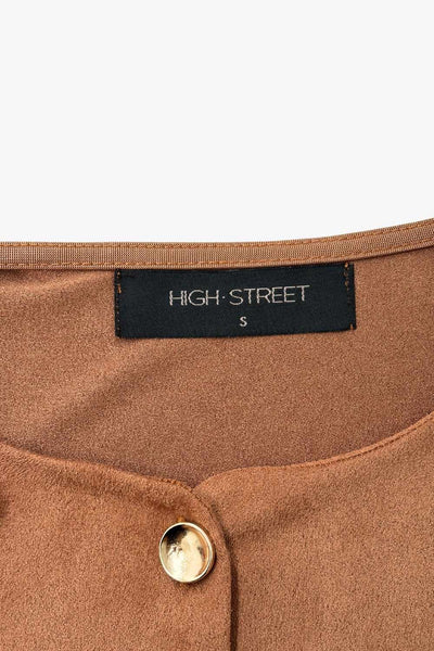 Chaleco corto de gamuza, fit recto, cuello redondo y cierre frontal con hilera de botones en contraste. Detalle de abertura frontal en bajo.