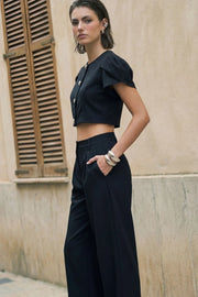 Blusa corta de fit recto, manga corta amplia con abertura, olanes y plisados en hombros, cortes frontales con pinzas, cuello redondo y cierre frontal con hilera de botones en contraste.