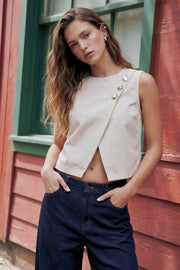 Top corto de fit recto, cuello redondo, sin mangas, cruce frontal en diagonal con botones decorativos en contraste, cierre posterior con botón y ojal.