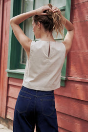 Top corto de fit recto, cuello redondo, sin mangas, cruce frontal en diagonal con botones decorativos en contraste, cierre posterior con botón y ojal.