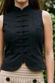 Top corto de fit ajustado, sin mangas, cuello mao, cierre frontal con botones y bajo frontal curveado.