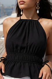 Top corto de cuello halter con plisados, tirantes delgados, detalle de rib con plisados y lazos laterales en costados, peplum con olanes en bajo y cierre posterior con botón y ojal.