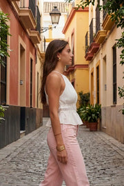 Top corto de cuello halter con plisados, tirantes delgados, detalle de rib con plisados y lazos laterales en costados, peplum con olanes en bajo y cierre posterior con botón y ojal.