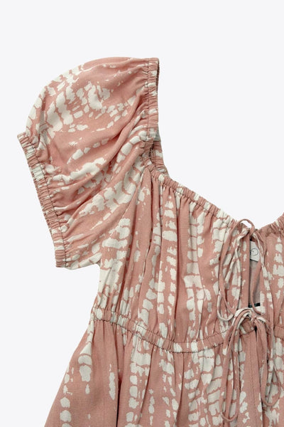 Top estampado de fit fluido, manga corta abullonada con rib elástico en bordes, escote redondeado con plisados, doble lazo amarrable y cut out frontal. Detalle de rib elástico en cintura y peplum con olanes en bajo.