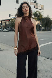 Blusa halter satinada de fit fluido, cuello halter fluido, sin mangas, bajo asimétrico con abertura lateral y encaje decorativo en contraste. Detalle de escote fluido en espalda, cierre posterior con botón y ojal.