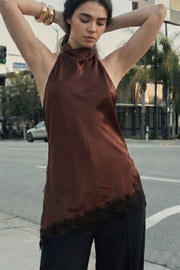 Blusa halter satinada de fit fluido, cuello halter fluido, sin mangas, bajo asimétrico con abertura lateral y encaje decorativo en contraste. Detalle de escote fluido en espalda, cierre posterior con botón y ojal.