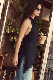 Blusa larga de fit fluido, sin mangas, cuello halter fluido, escote en espalda, bajo asimétrico con encaje en borde y aberturas laterales. Cierre posterior con botón y ojal.