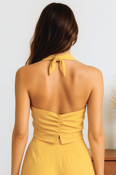 Top corto de cuello halter con nudo amarrable posterior, fit ajustado, escote v, cierre frontal con hilera de botones y bajo v frontal. Escote en espalda y detalle de plisado posterior.