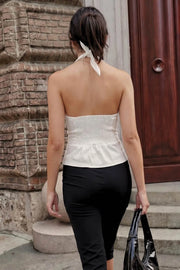Top corto de cuello halter con nudo amarrable posterior, escote v con cortes y plisados decorativos frontales, fit ajustado, escote en espalda con fruncido posterior, cierre frontal con hilera de botones y bajo curveado con abertura.