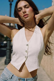 Top corto de cuello halter con nudo amarrable posterior, fit ajustado, escote v, cierre frontal con hilera de botones y bajo v frontal. Escote en espalda y detalle de plisado posterior.
