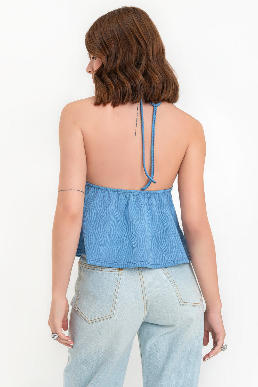 Top corto halter de escote v con lazo amarrable frontal, rib elástico en espalda, tirantes halter con lazo amarrable posterior y abertura frontal en bajo. Detalle de peplum olanes y textura en tejido.