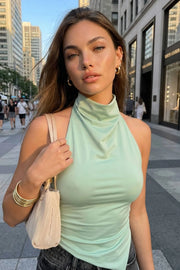 Top halter corto de fit ajustado, sin mangas, cuello halter fluido con plisados y escote en espalda. Detalle de bajo diagonal asimétrico.