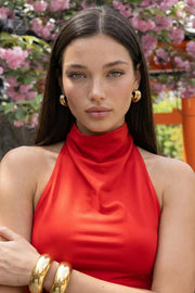 Top halter corto de fit ajustado, sin mangas, cuello halter fluido con plisados y escote en espalda. Detalle de bajo diagonal asimétrico.
