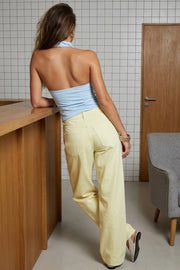 Top halter corto de fit ajustado, sin mangas, cuello halter fluido con plisados y escote en espalda. Detalle de bajo diagonal asimétrico.