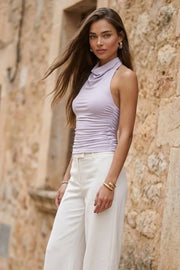 Top halter de fit ajustado, cuello alto fluido, sin mangas, plisados en costados y cierre posterior con botón y ojal.