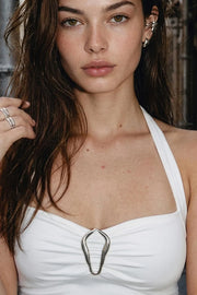 Top de fit ajustado, cuello halter con lazo amarrable posterior, escote con cortes, plisados y hebilla decorativa en contraste. Detalle de bajo asimétrico frontal.