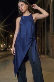 Blusa larga satinada de fit fluido, cuello halter, sin mangas, bajo asimétrico, plisados en costado con abertura y nudo decorativo , cierre posterior con botón y ojal.